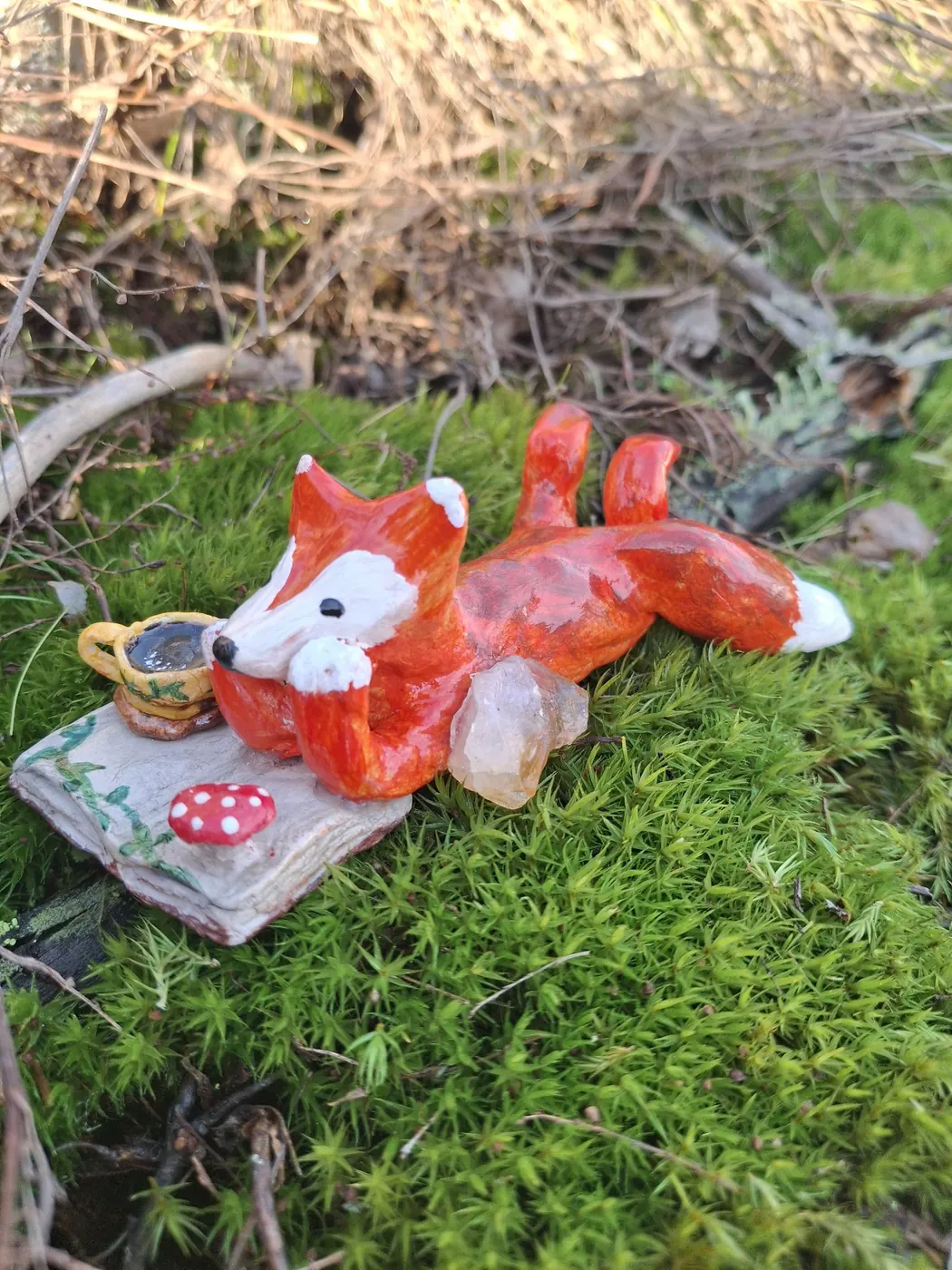 Kettu makaa sammaleella kirjan päällä teekupin ja kristallin vieressä